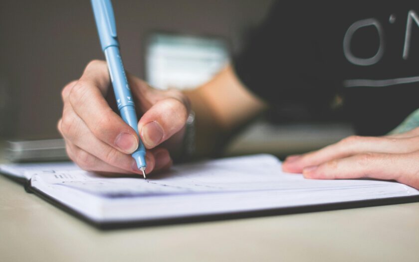 Close-up of hand writing in notebook using a blue pen, focus on creativity.