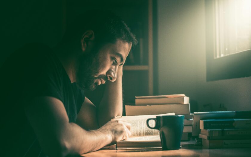 An adult man immersed in reading by the window in Madrid. Warm, focused study atmosphere.