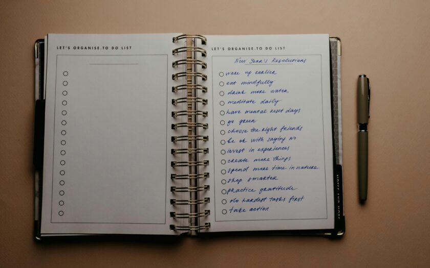 Open planner with New Year's resolutions, spiral binding, and pen on warm-toned background.